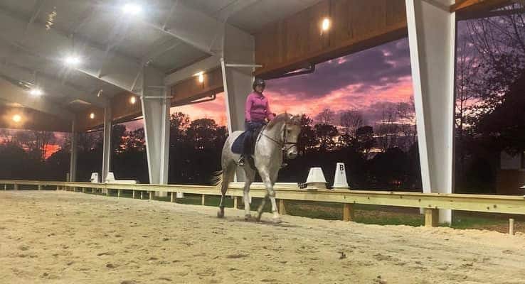 Rider on a horse in covered arena at sunset.